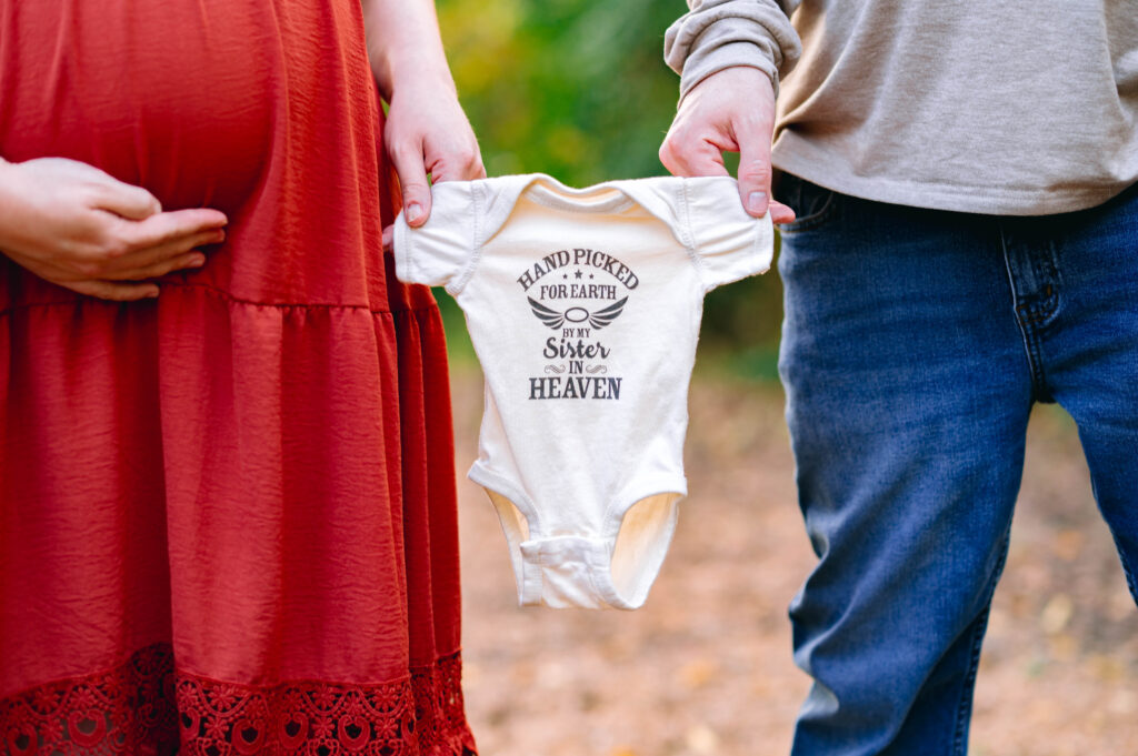 Parents holding a baby onesie during McKinney maternity photos, symbolizing anticipation and connection before welcoming their newborn.