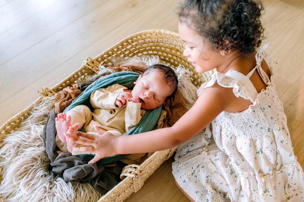 Big sister gently touching her newborn sibling’s feet during a McKinney newborn photography session, capturing sibling connection and newborn details.