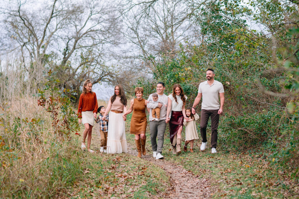 Extended family walking hand in hand down a wooded trail during a candid outdoor fall photo session at Erwin Park in McKinney.