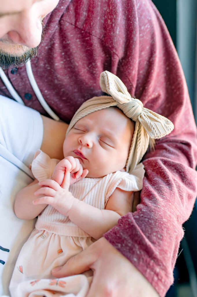 Mom and dad holding newborn daughter with dad looking at daughter for their in home lifestyle newborn session in McKinney, Texas, by a McKinney Newborn Photographer.
