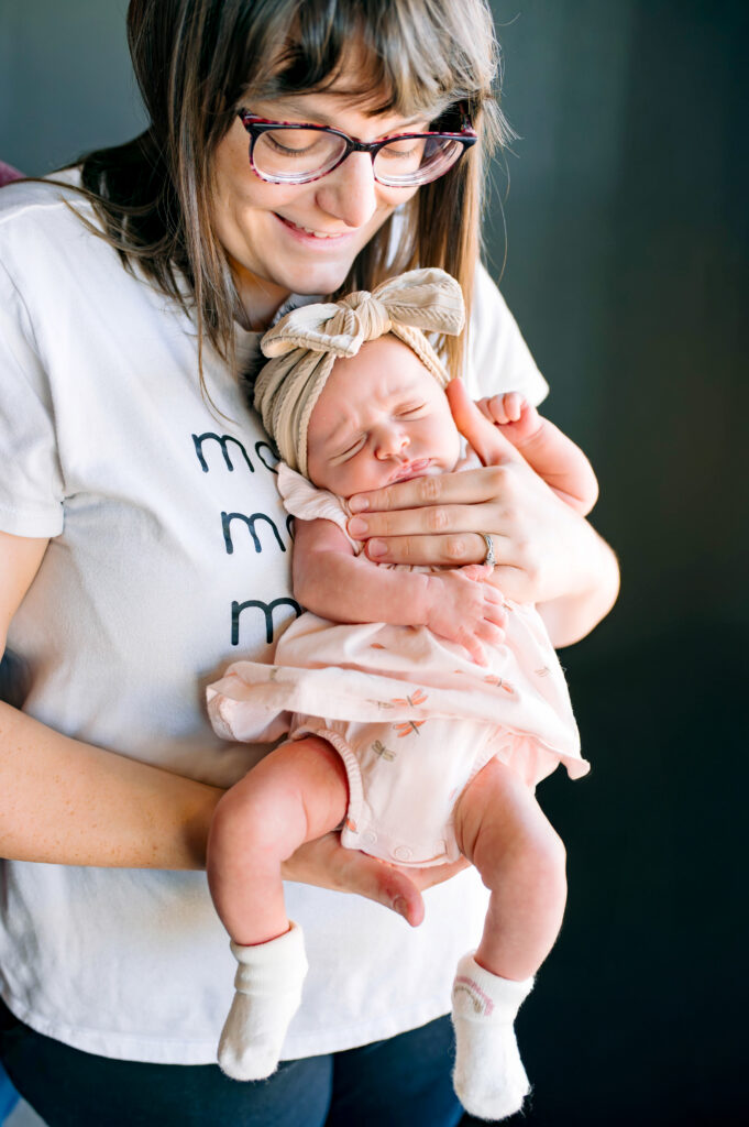Mom holding newborn daughter with baby looking out for their in home lifestyle newborn session in McKinney, Texas, by a McKinney Newborn Photographer.