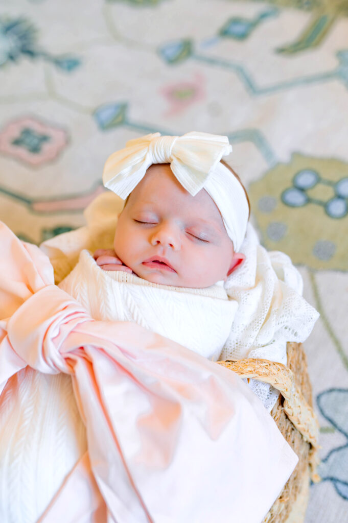 Baby girl in basket asleep wrapped in white with pink bow during newborn session in Murphy, Texas. 