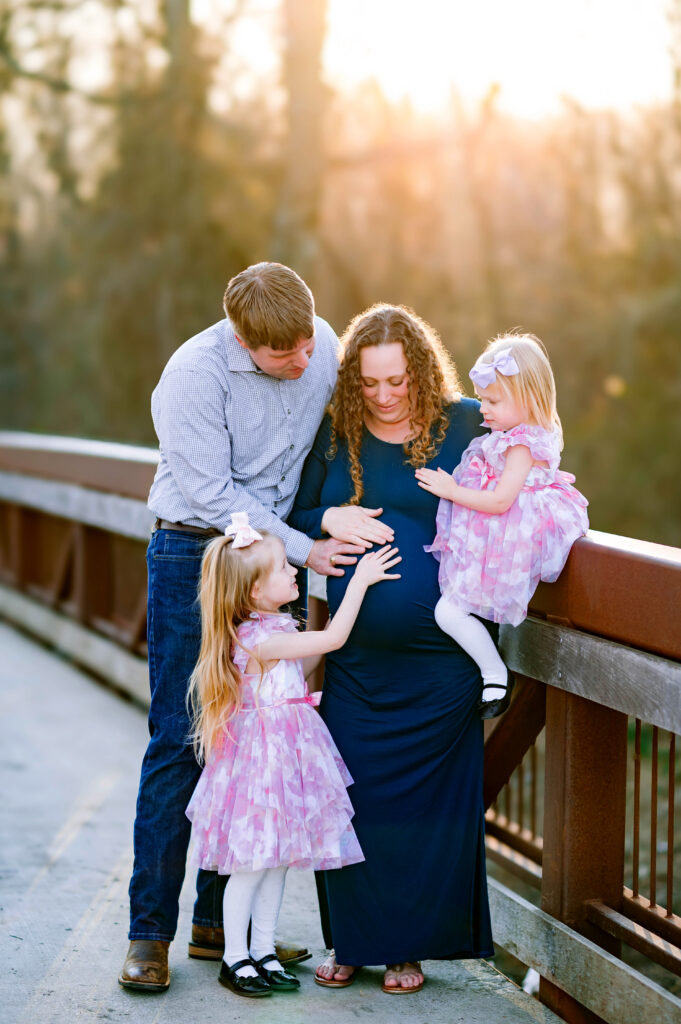 Plano maternity photographer capturing parents and sisters touching moms belly at Oak Point Nature Preserve in Plano, Texas for a maternity session in Plano, Texas.