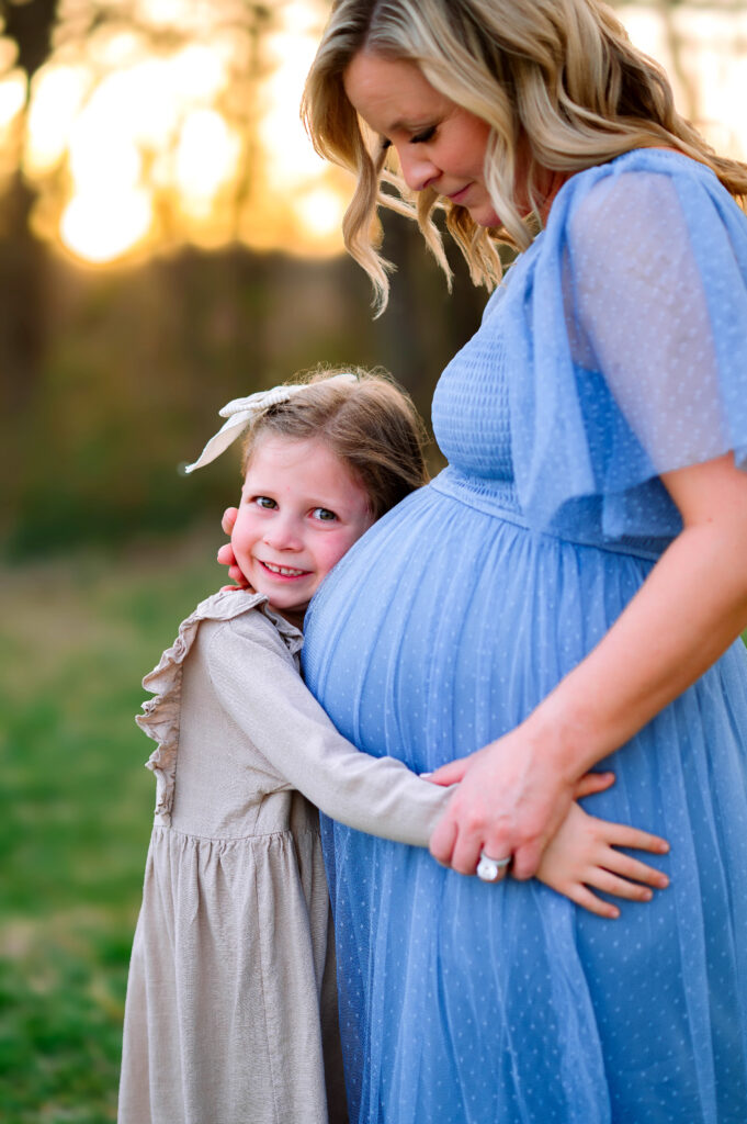 Daughter hugging pregnant mom at Oak Point Park in Plano, Texas, during a maternity session with Plano Maternity Photographer. 