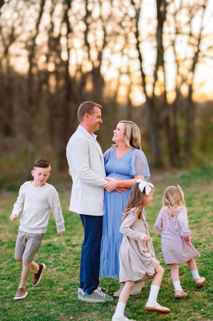 Family of five running around pregnant mom and dad at Oak Point Park in Plano, Texas, during a maternity session with Plano Maternity Photographer. 