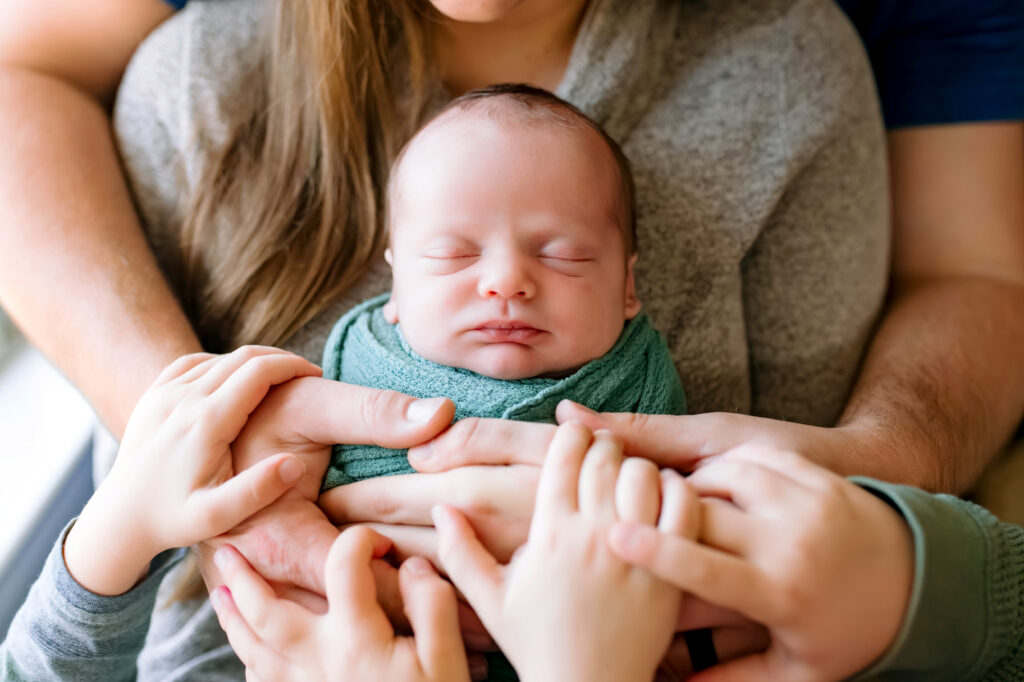 Baby asleep in mothers arms with families hands on babies chest during newborn session in Rockwall, Texas.