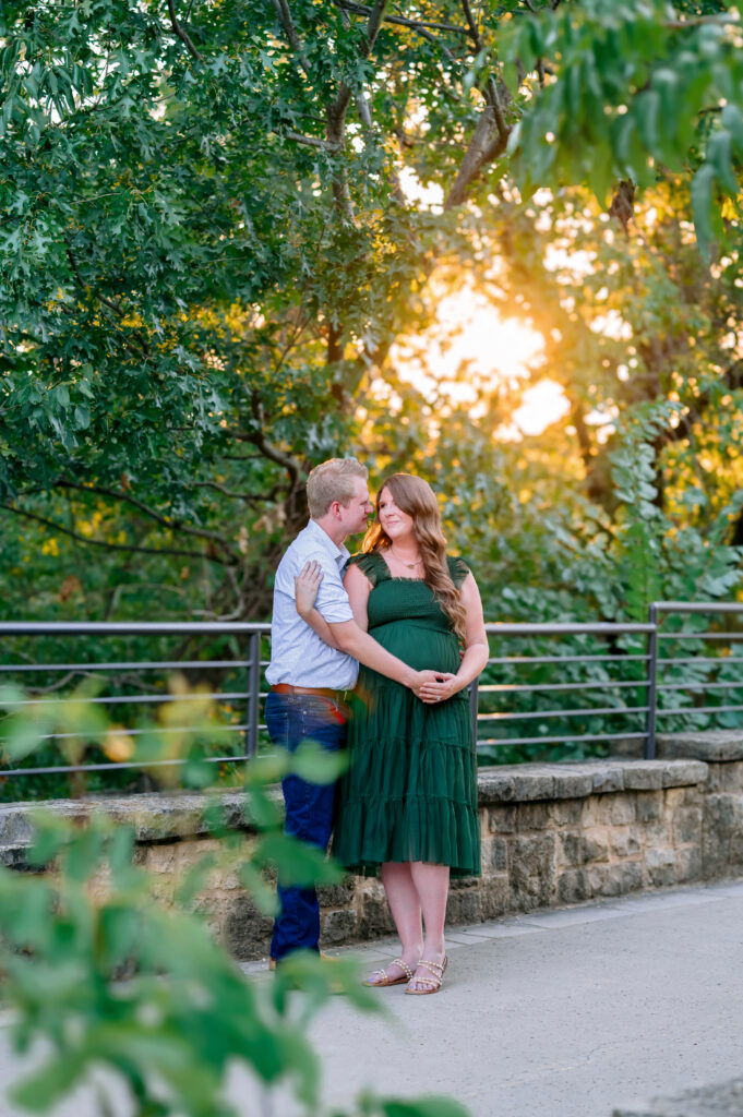 McKinney maternity photographer capturing pregnant mom and dad on bridge with sun glare at Arbor Hills for a maternity session in Plano, Texas.
