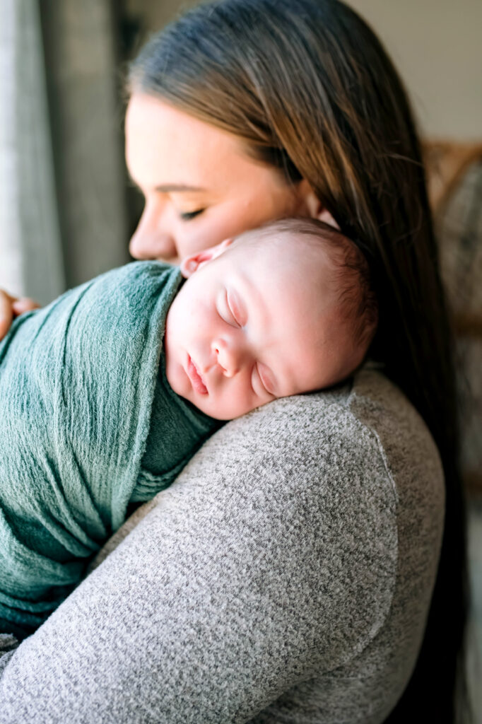 Baby boy wrapped in green asleep on mom's shoulder during newborn session in Rockwall, Texas.