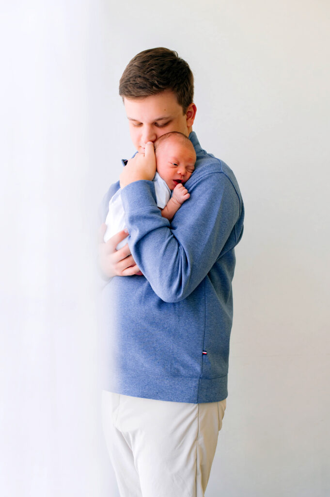McKinney newborn photographer capturing dad holding newborn boy in a bright studio for their newborn session in McKinney, Texas.