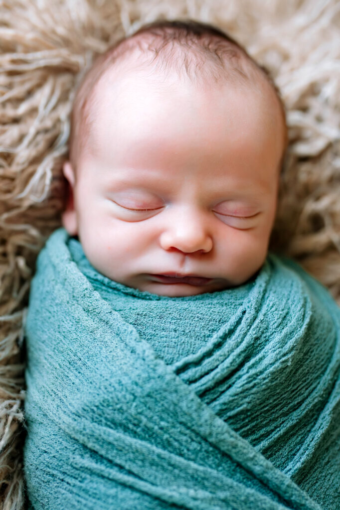 Baby boy wrapping in green on fur blanket asleep during newborn session in Rockwall, Texas.