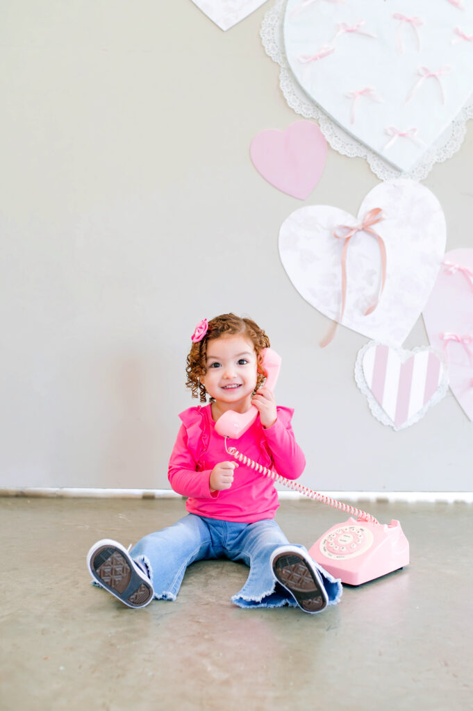 Valentine’s Mini Session child portrait in McKinney Texas with pink heart decor and vintage pink phone