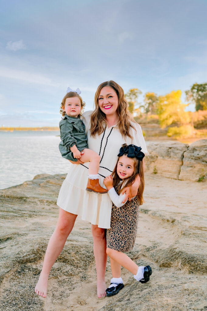 Mom holding 2 daughters standing on a rock for a mini family session at Murall Park in Flower Mound Texas.