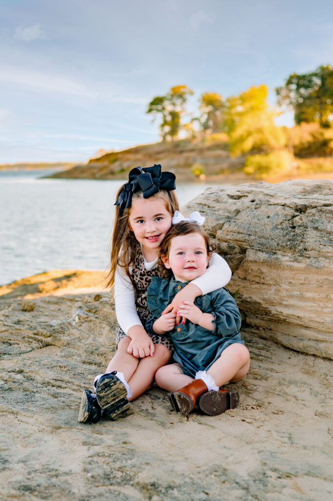Little sisters sitting on a rock for a mini family session at Murall Park in Flower Mound Texas.