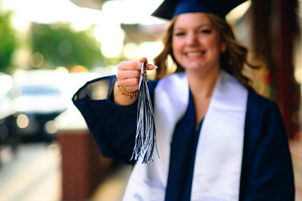 Teenage girl in cap and gown in downtown McKinney Texas holding her tassel for her senior photoshoot with Jennifer L Kirk Photography. 