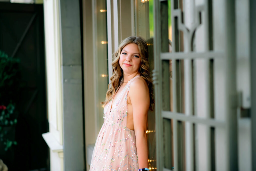 Teenage girl in a dress in front of a store window in downtown McKinney Texas for her senior photoshoot with Jennifer L Kirk Photography. 