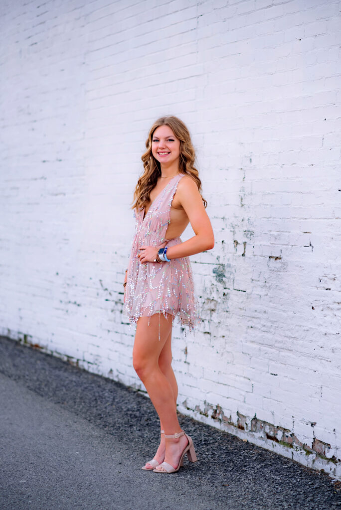 Teenage girl in a dress in downtown McKinney Texas with a white brick wall behind her for her senior photoshoot. 