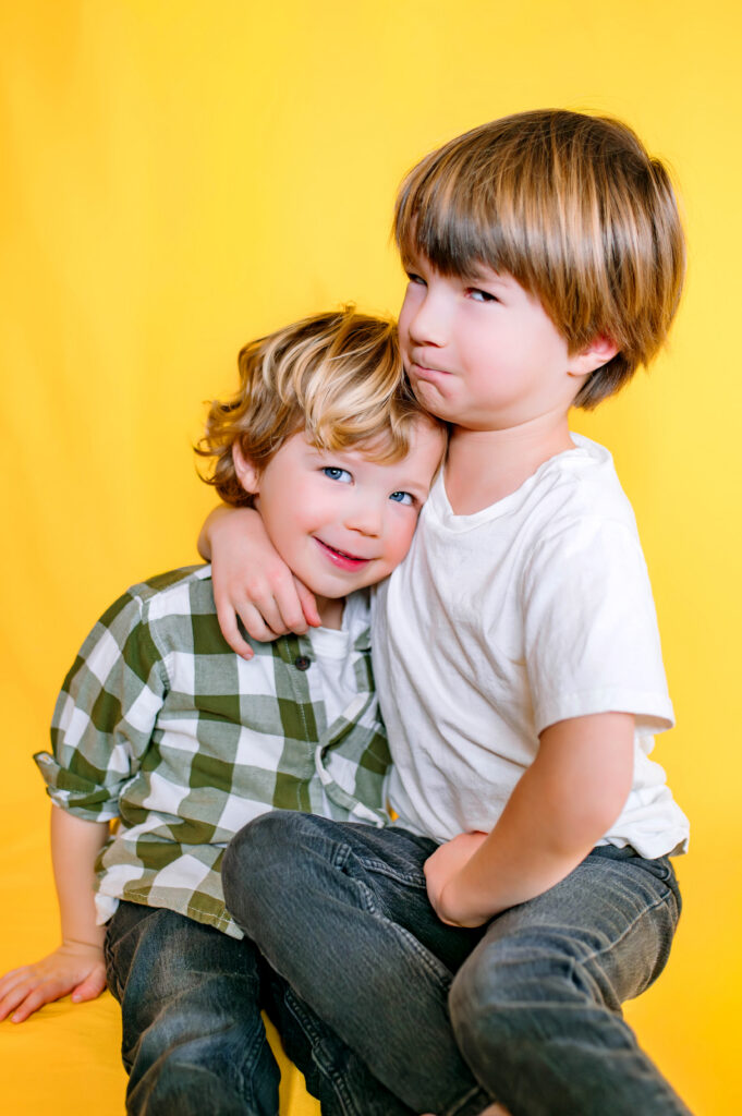 Brothers hugging each other smiling  in front of yellow backdrop for personality pictures in Wylie, Texas. 