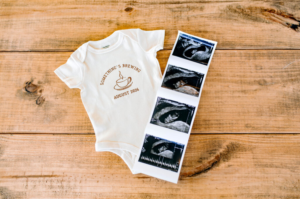 Picture of baby onesie and baby sonogram on wood table during a coffee shop birth announcement photoshoot in Rockwall, Texas. 