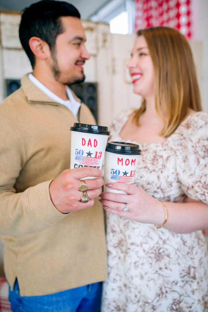 Mom and dad looking at each other while hold to go coffee cups that day mom and dad during their birth announcement session with Jennifer L Kirk photography in Heath, Texas. 