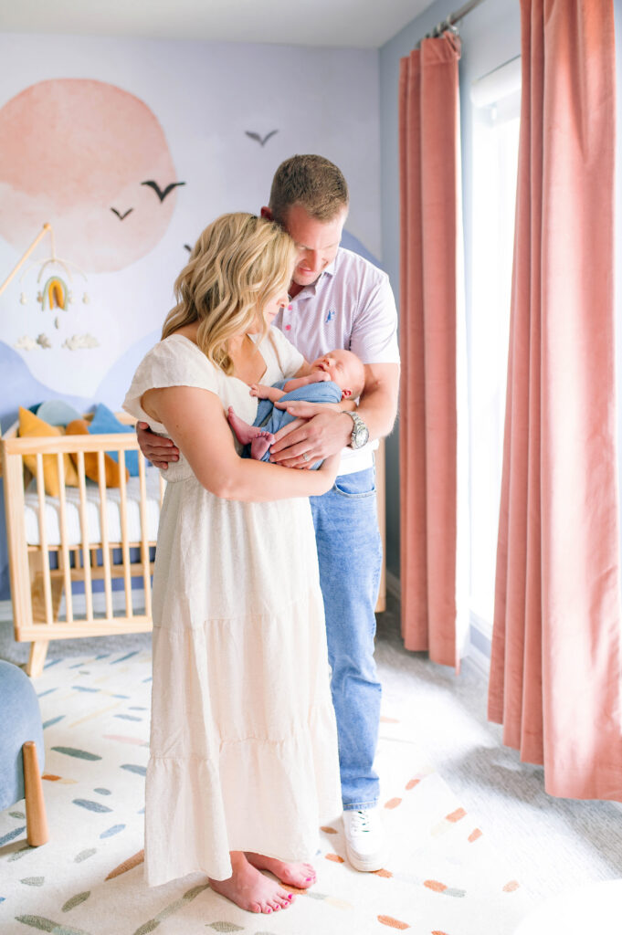 Mom and dad holding and looking down at newborn son in baby nursery during newborn session with Jennifer L Kirk Photography in Plano, Texas. 