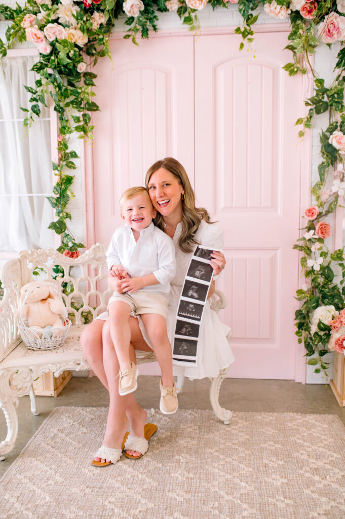 Mother and toddler announcing pregnancy while holding ultrasound photos during a birth announcement session at Lemon Drop Studios in McKinney, Texas.