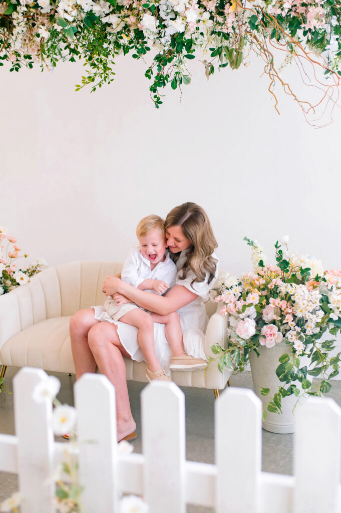 Mother laughing and cuddling her young son during a spring birth announcement photo session at Lemon Drop Studios in McKinney, Texas.