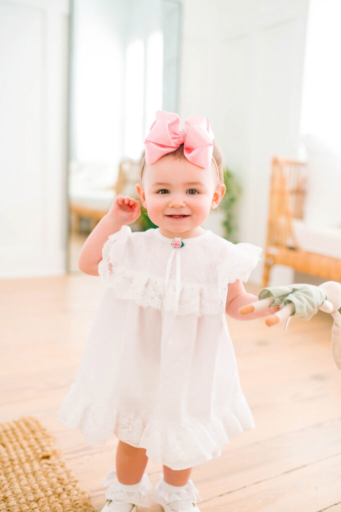 Little girl in white dress smiling and standing during a mommy and me portrait session in Mckinney, Texas.