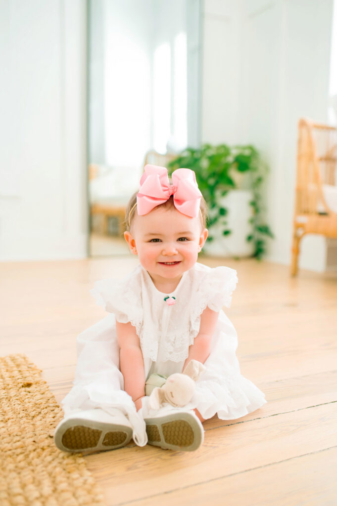 Little girl in white dress smiling and sitting during a mommy and me portrait session in Mckinney, Texas.