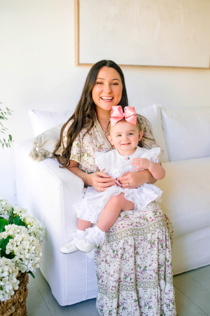 Mom and toddler girl smiling at camera sitting on a white couch during a mommy and me session in Mckinney, Texas. 