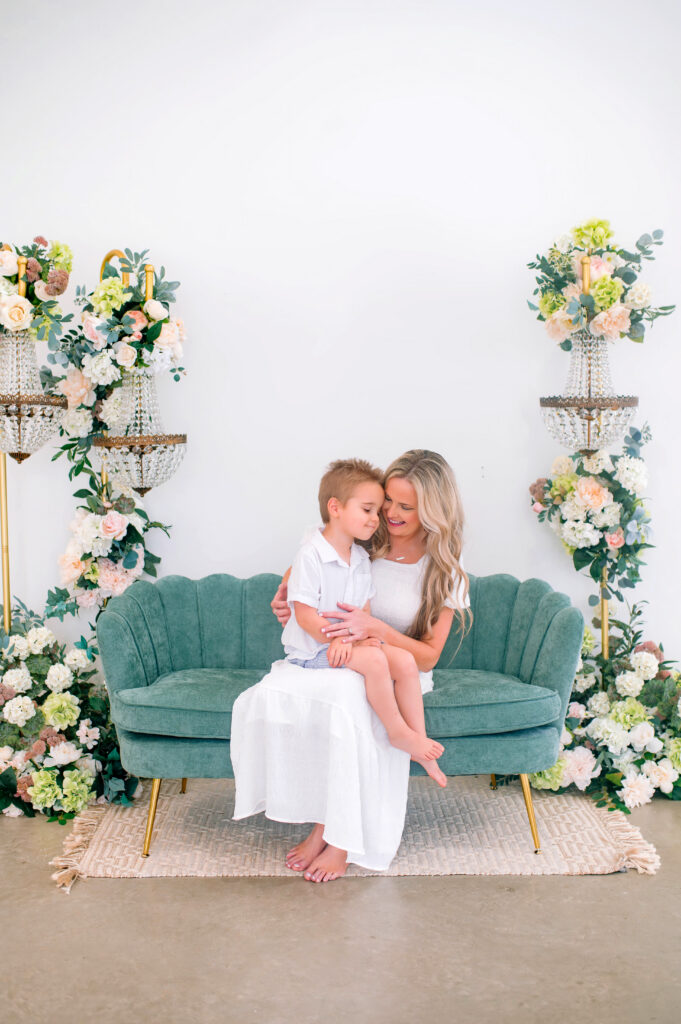 Little boy sitting on moms lap sitting on a green couch during a spring mommy and me photography session at Lemondrop Studios in Mckinney, Texas. 