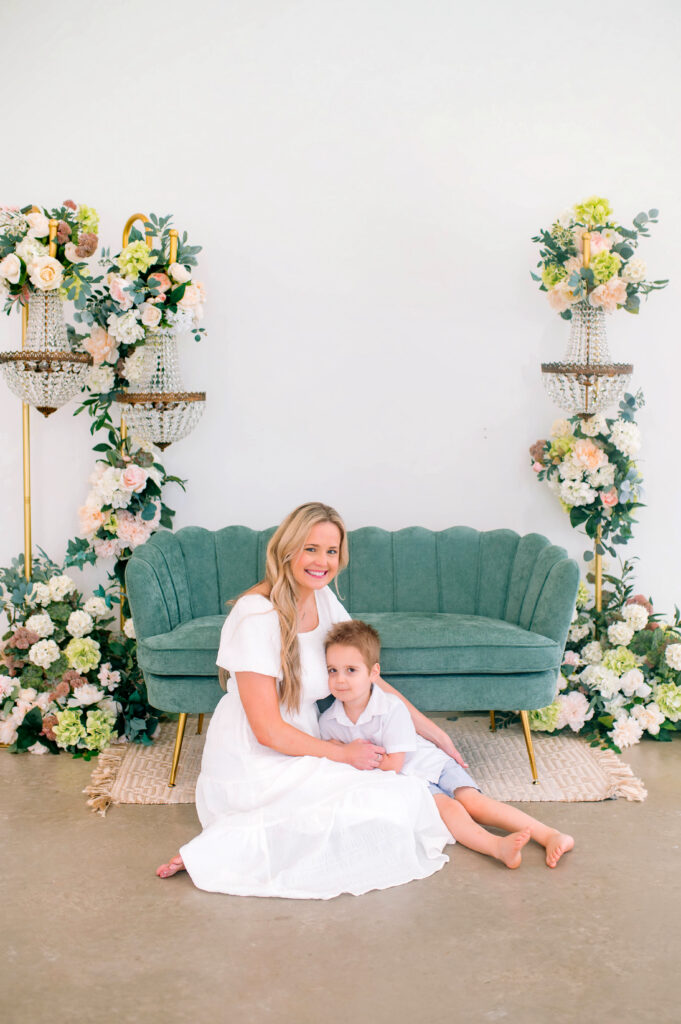 Mom and son sitting on floor in front of green house during a spring portrait session at Lemondrop Studios in Mckinney, Texas. 