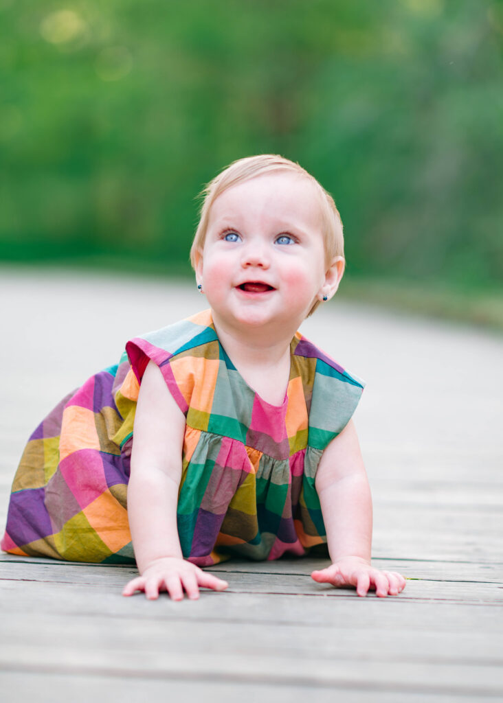 Baby girl crawling and smiling on a wooden path at Oak Point Nature Preserve in Plano, Texas. 