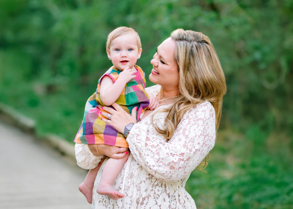 Baby girl held by her mom who is smiling at her during their family session at Oak Point Nature Preserve in Plano, Texas. 