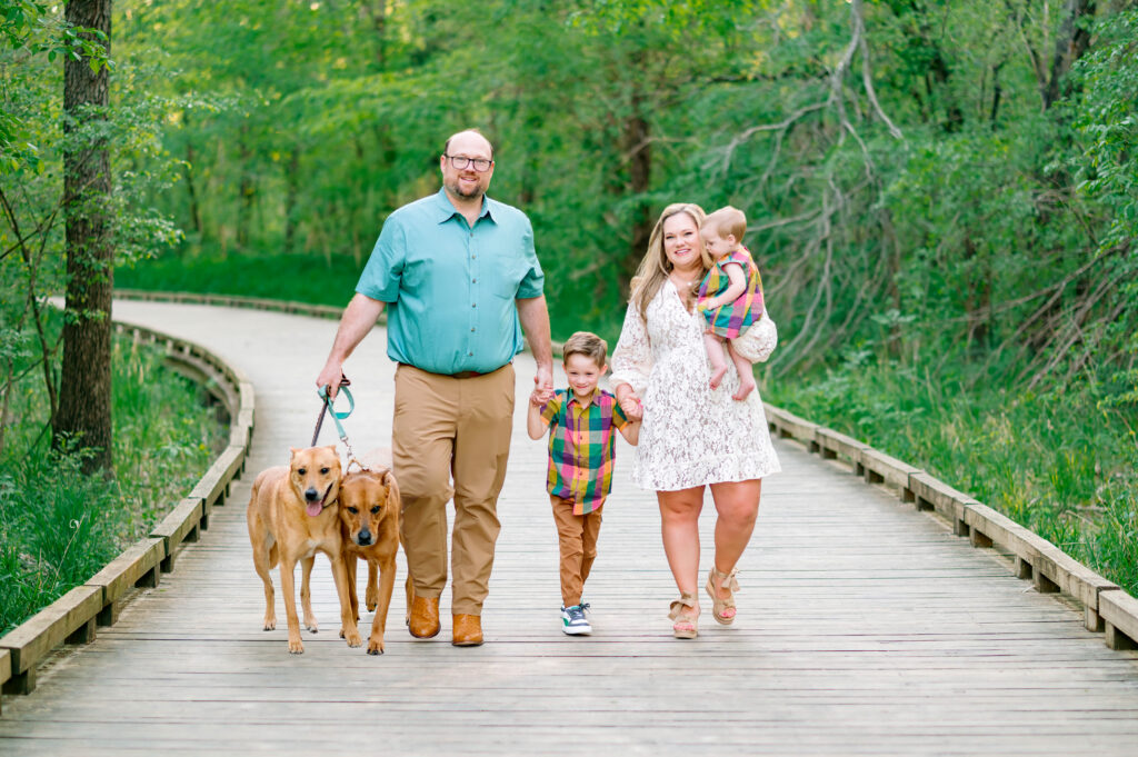 Family walking their dogs on wooden path during their family session in Plano, Texas. 